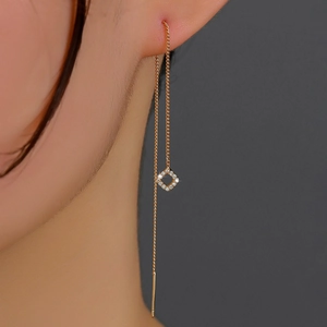 Close-up of elegant gold tassel earrings with glittering zircon square pendant on ear