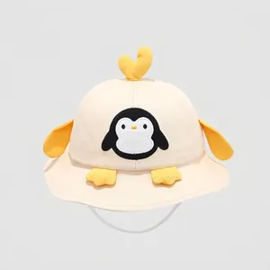 Dettaglio ravvicinato di un cappello a secchiello in cotone crema con simpatico pinguino 3D
