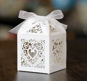 Detailed view of white laser-cut heart pattern wedding candy box with a ribbon bow
