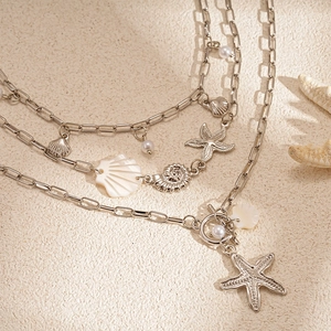 Close-up of triple-layered silver necklace with starfish and shell pendants on sand