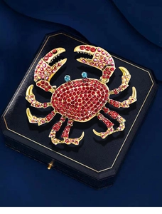Detailed macro view of crab brooch with vibrant red rhinestones on a navy velvet box
