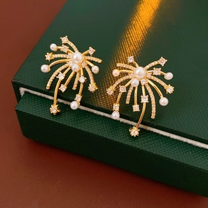 Close-up of 18K gold fireworks earrings with pearls on a dark green gift box