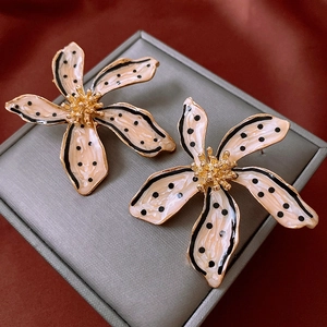 Macro detail of enamel flower earrings with black polka dots and gold metallic edges
