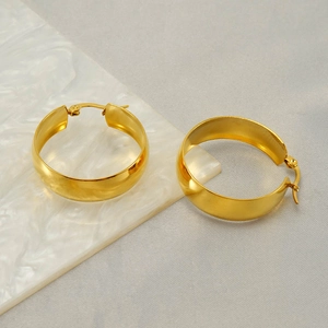 Detail shot of wide gold hoop earrings on marble, highlighting the polished finish