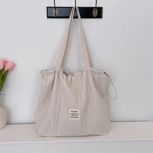 Detail of cream pleated tote bag with fabric logo label hanging on a wall hook