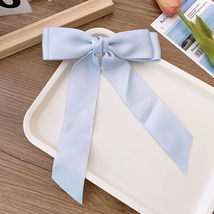 Detail of light blue satin bow hair clip with long ribbons on a white tray
