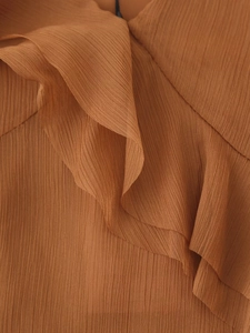 Détail de la robe asymétrique orange brûlé avec plis verticaux et volants superposés