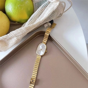 Macro detail of gold oval quartz watch with elegant metal link strap on stylish tray