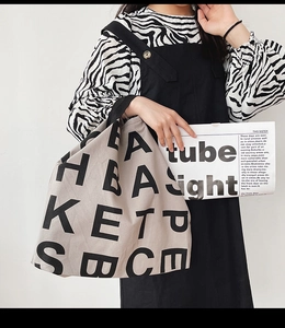 Detail of minimalist beige canvas tote bag with black letter print held by a model