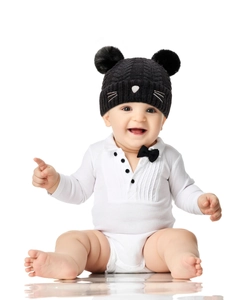 Detail of baby knit hat with pom poms and matching white onesie with black bow tie