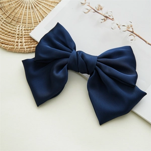 Close-up of a large navy blue satin bow hair clip on a white background with cotton stems