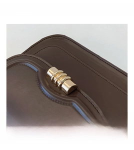 Detailed close-up of dark brown leather crossbody bag with golden wavy metal clasp