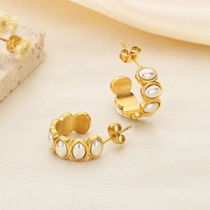 Detail of 18k gold stainless steel C-shaped earrings with white pearls on a soft background
