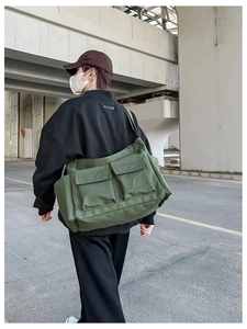 Detail view of army green canvas messenger bag with large pockets on back of model