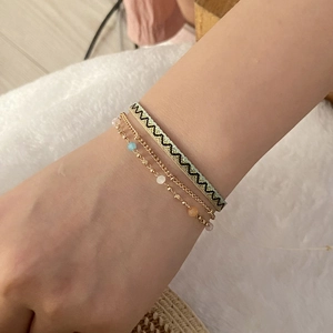 Bohemian style bracelet set with green woven ribbon and gold beaded chains on wrist