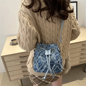 Blue tie-dye denim bucket bag with frayed patch details worn by a model in casual style