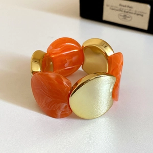 Chunky elastic bracelet featuring marbled orange resin and polished gold-tone metal blocks