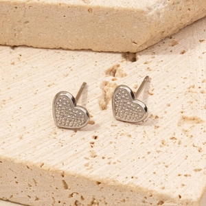 Close-up of heart-shaped silver earrings with textured finish on natural stone