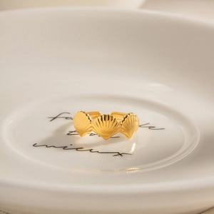 Detailed view of an 18k gold scallop shell open ring on a decorative white ceramic dish