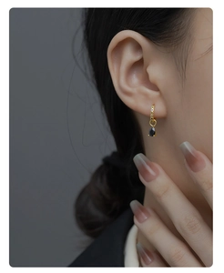 Close-up of a model wearing a gold teardrop earring with black stone and colorful crystals