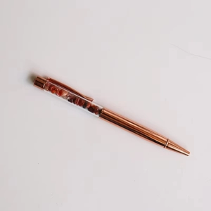 Detail of rose gold metal ballpoint pen featuring crushed red stone crystal filler