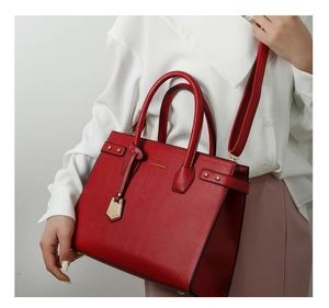 Detailed view of red lychee grain leather handbag with gold logo and shoulder strap