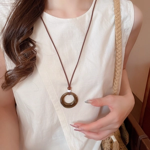 Close-up of amber resin circle pendant on white linen shirt with minimalist brown cord