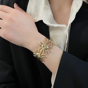 Nahaufnahme eines goldenen Armreifs mit Sonnendesign, getragen zu Schwarz-Weiß-Kleidung.