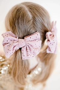 Detail of pink embroidered eyelet bow hair ties worn on a girl's pigtails
