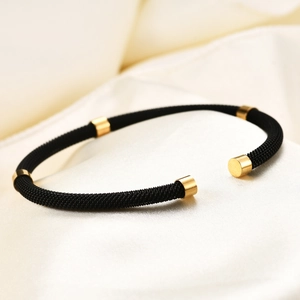 Close-up of black braided stainless steel cable bracelet with gold cylinder accents