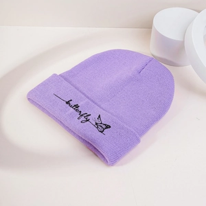 Gros plan d'un bonnet tricoté violet avec broderie papillon noire sur surface blanche