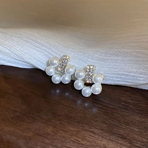 Detail of floral pearl earrings with gold metal frame and rhinestones on dark wood surface