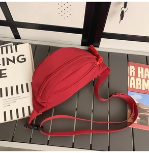 Detail view of red canvas crossbody bag with multiple zippers and woven cord pullers