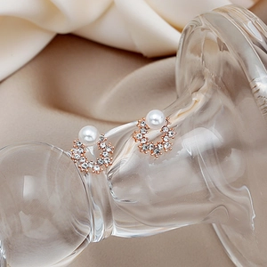 Close-up of rose gold pearl stud earring with pavé rhinestones on silk background