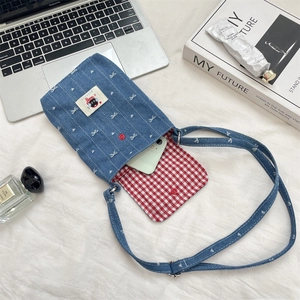 Detail van blauwe denim telefoontas met wit strikborduursel en rood geruite voering