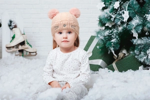 Detail of baby knit hat with pink pom-poms and cute cat embroidery in winter setting