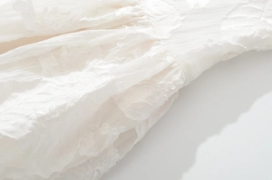 Close-up of white dress fabric showing intricate floral embroidery and pleated texture details