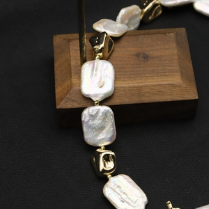 Baroque pearl necklace with gold geometric beads on dark wood and black background