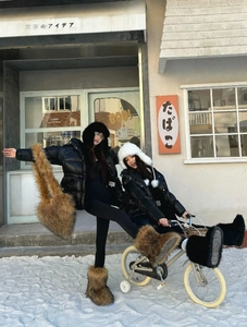 Asian model wearing oversized faux fur earmuff hat and shiny black down jacket in snow