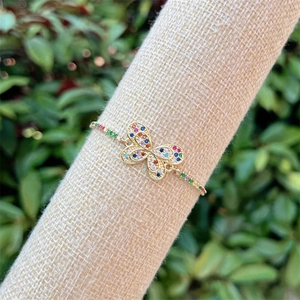 Close-up of 18k gold butterfly bracelet with colorful zircon pavé on a linen stand