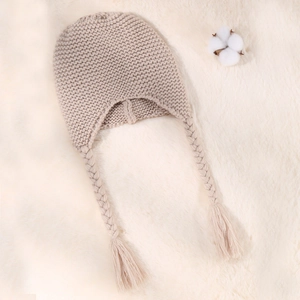 Detail of knitted baby hat with braids and soft cotton decor on white fur background