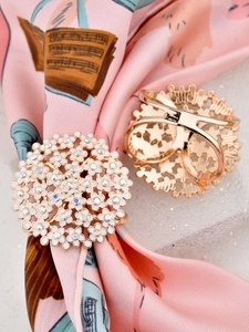 Close-up of golden rose enamel and rhinestone scarf rings on floral printed silk fabric