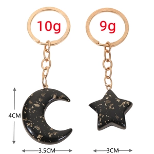 Detail view of star and moon keychains in black resin with gold foil including dimensions