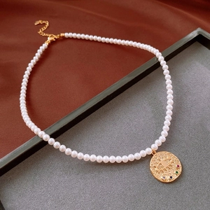 Detail view of pearl necklace featuring a textured gold coin pendant with colorful gems