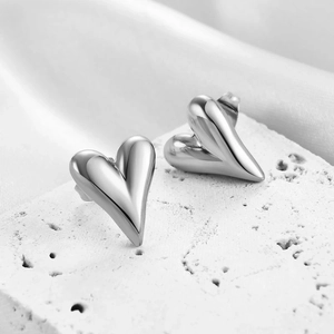 Polished silver heart stud earrings on white stone and satin background for women