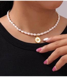 Detail of freshwater pearl necklace with gold oval shell pendant on model's neck