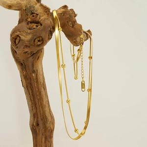 Zweilagige 18K vergoldete Edelstahl-Schlangenkette mit Perlen auf einem Holzast