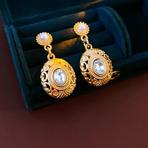 Macro shot of vintage gold-plated oval earrings with clear zircon and pearl in velvet box