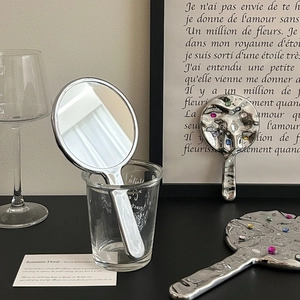Silver handheld makeup mirrors with gemstones and textured metal finish in a chic setup