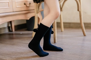 Detail of black high-elastic knitted baby knee-high socks with cute pompom bow accents